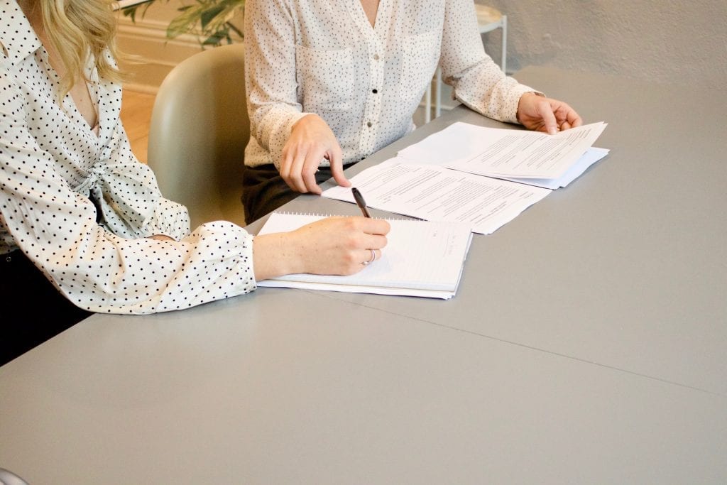 Woman writing on white paper beside another woman handling other papers
